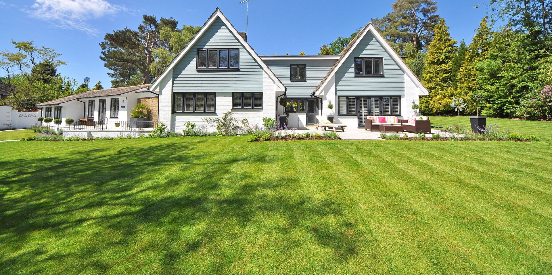 stunning large white house with a vast well-manicured lawn area, surrounded by trees and bushes, with a clear blue sky