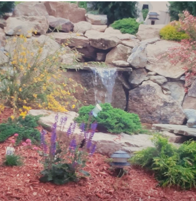 A small waterfall on personal property created with an assortment of rocks with surrounding yellow and purple florals
