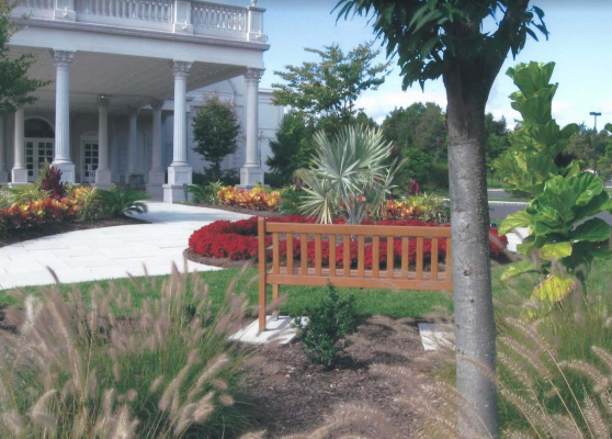 Tropical style landscaping accomplished in New Jersey at a palatial white pillared home with a brown bench