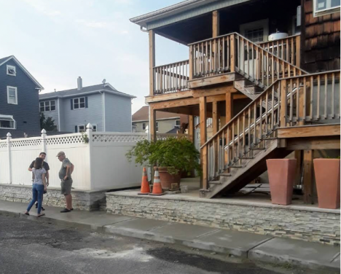 3 people standing outside of a building with multi levels of stairs; large plants in pots on the walkway