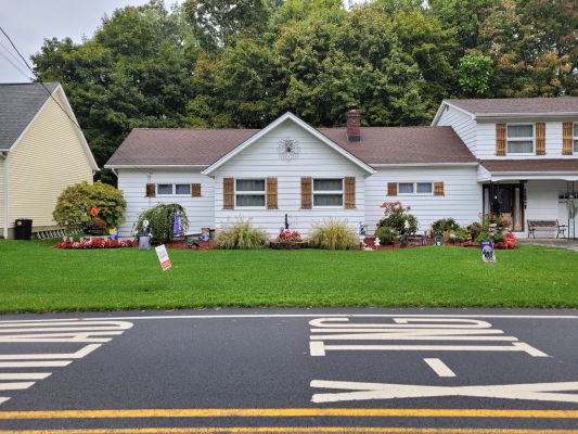 a modest white home with lush well manicured lawn and various shrubbery unique planted around the house