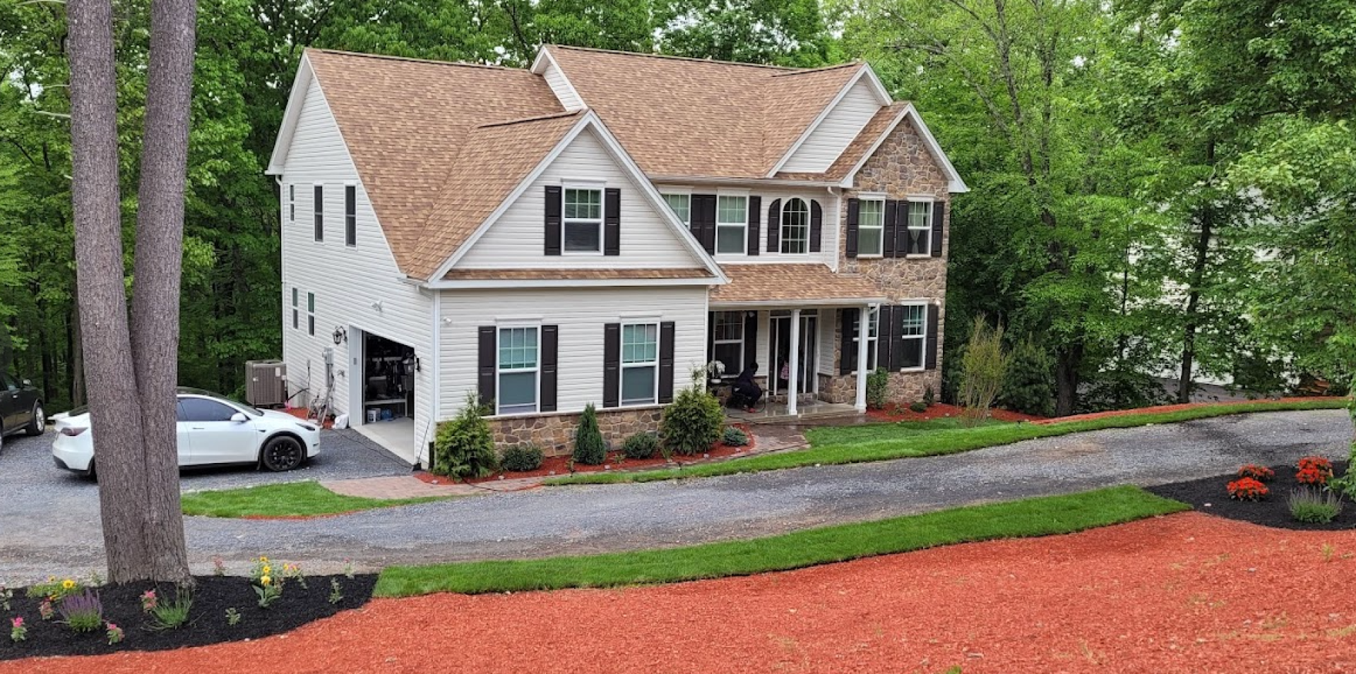 A spacious white house surrounded by lush green trees and well-manicured lush lawn and colorful florals